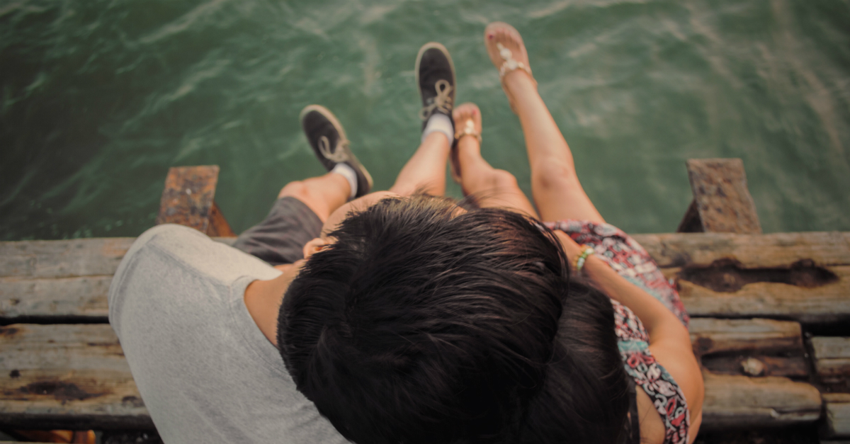 couple sitting on deck with feet over water, ready to marry